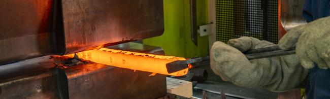 Glowing metal block is forged with hydraulic press.