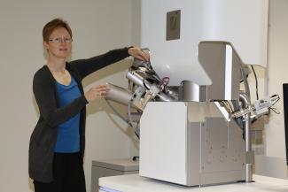 Stehende weibliche Person neben einem Rasterelektronenmikroskop