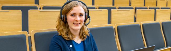 Eine junge Frau mit Laptop und Headset im Hörsaal