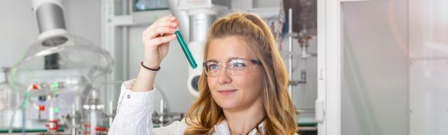 Eine Studentin betrachtet eine Flüssigkeit im Reagenzglas