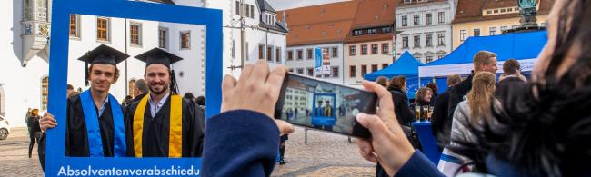 Zwei Absolventen lassen sich mit einem großen Fotorahmen der Universität fotografieren