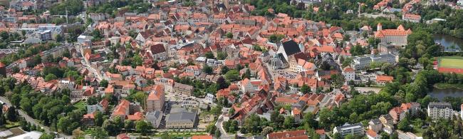 Luftbild einer Kleinstadt mit roten Ziegeldächern. Eine kreisförmige Altstadtstruktur ist erkennbar.
