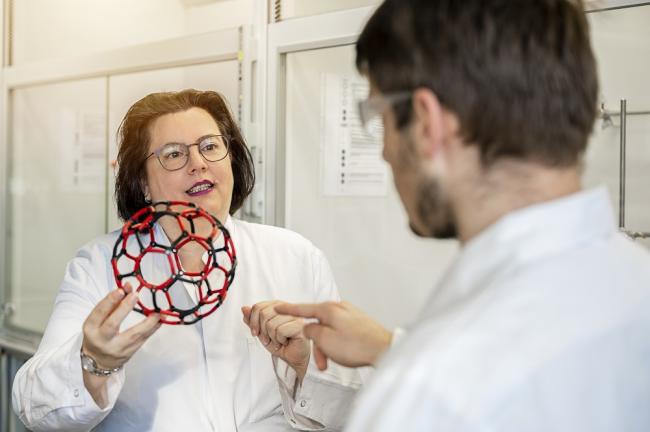 Das Bild zeigt eine Frau und einen Mann, die sich über ein ballförmiges Modell unterhalten, das die Frau in den Händen hält. 