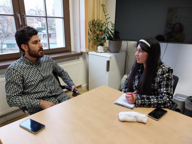 A young male scientists in conversation with a school student. Both of them sitting a table in a meeting room.