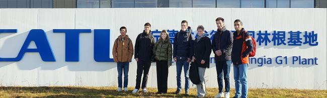 Die Exkursionsgruppe steht vor einer Wand mit dem Schriftzug "CATL". Im Hintergrund ist die Glasfassade eines Gebäudes zu sehen.