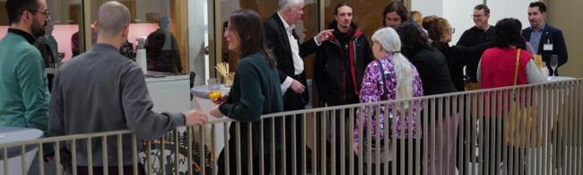 Personen stehen mit Gläsern in der Hand im Treppenhaus.