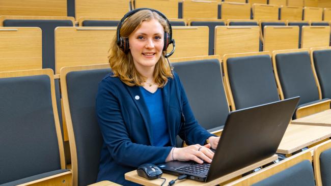 Eine junge Frau mit Laptop und Headset im Hörsaal