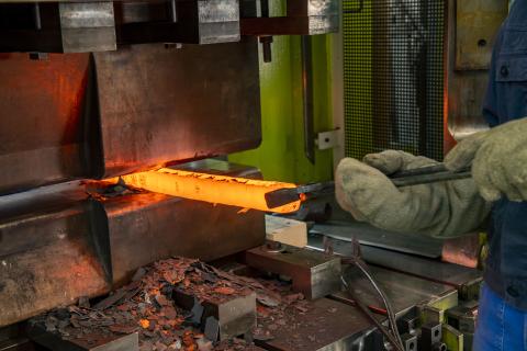 Glowing metal block is forged with hydraulic press.