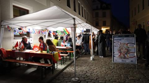Ein Gespräch am beleuchteten Stand &quot;Language Corner&quot;, der Titel ist auf einem großen Aufsteller zu lesen