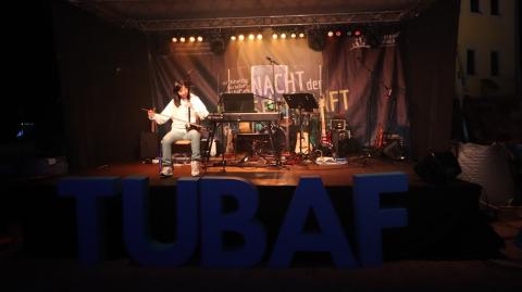 Eine chinesische Frau sitzt auf einer Bühne und spielt eine chinesische Kniegeige, die sie auf ihren Oberschenkel gestellt hat