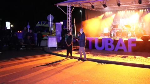 Der Moderator der Bühnenshow spricht mit einer indischen Studentin vor der Bühne, umgeben von orangefarbenem Licht