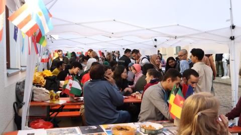 Eine große Anzahl von Besuchern sitzt auf Bänden an Festzelttischen, Länderfahnen schmücken die Stände