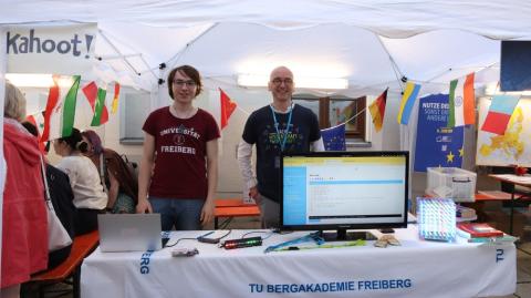 Ein junger Student und ein Dozent an einem Stand mit Computermonitor, auf dem Programmcode zu sehen ist