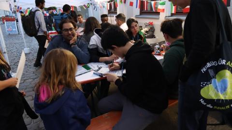 Am Stand &quot;Schreibe deinen Namen&quot;: Ein chinesischer Student schreibt für ein Mädchen deren Namen auf