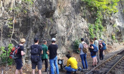 Studierende an einem gesichterten Felsaufschluss neben einer Schmalspurbahnstrecke