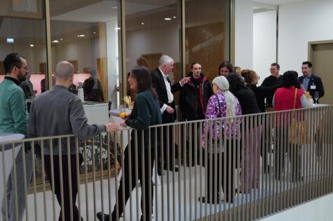 Personen stehen mit Gläsern in der Hand im Treppenhaus.