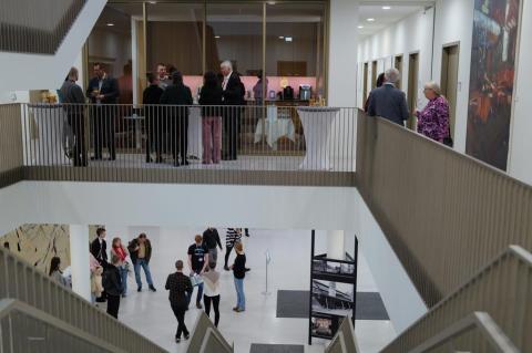 Personen stehen mit Gläsern in der Hand im Treppenhaus.