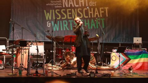 Ein Sänger auf einer Bühne mit einem Mikrofon in der Hand beim Singen. Seine Augen sind geschlossen.
