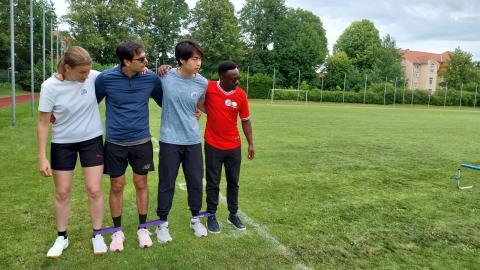4 Sportlerinnen und Sportler auf einem Rasenplatz bei einer sportlichen Challenge