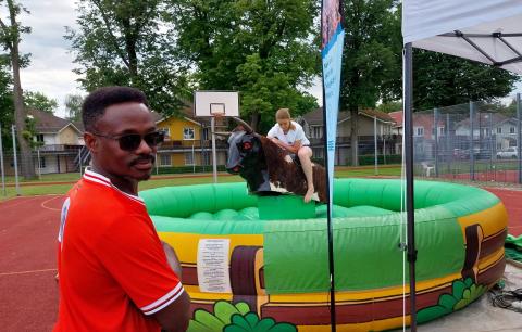 Die Station "Bullriding" mit grünem Luftkissenpolster, im Vordergrund ein Sportler in einem roten T-Shirt