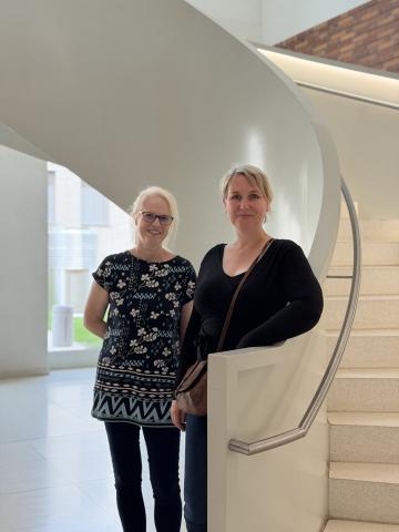 Zwei Frauen stehen vor einer weißen Wendeltreppe in einem hellen Innenraum
