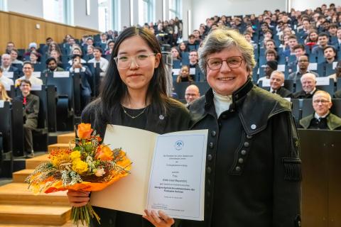 Eine Urkunde und ein Blumenstrauß werden einer jungen Frau verliehen