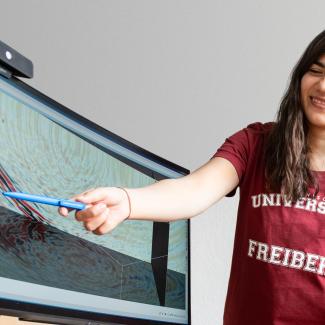 Zwei Studentinnen zeigen einem Dozenten etwas auf dem Bildschirm
