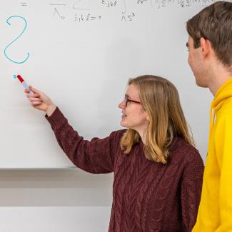 Drei Studierende stehen an einer Tafel und betrachten eine Formel