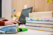 Schreibtisch mit Notebook, Büchern und einer Hand