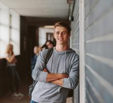 Ein junger Mann lehnt sich in einem Schulflur an eine Wand