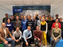 Studierende positionieren für Gruppenfoto bei BASF vor Leinwand, die das Werksgelände zeigt