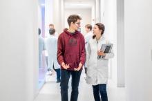 Student und Mitarbeiterin im Laborflur in wissenschaftlicher Diskussion