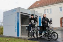 Zwei Studenten sitzen jeweils auf einem CityPed und befinden sich vor der CityBox am Audimax