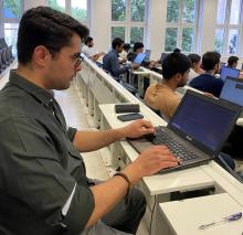 Junger Mann sitzt in einem Hörsaal, vor sich einen Laptop