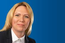 Portraitfoto einer blonden Frau im Anzug vor blauem Hintergrund