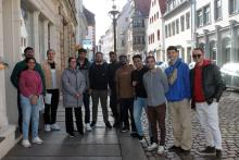 Eine Gruppe von 11 weiblichen und männlichen Studierenden aus verschiedenen Ländern auf einer Straße mit sanierten Altstadthäusern und Kopfsteinpflaster