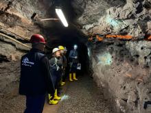 Fünf Leute mit Helmen und Gummistiefeln stehen im Bergwerk und begutachten einen Stolln.