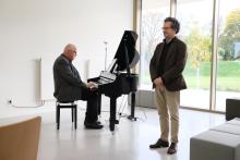 Ein Mann sitzt am Klavier und ein anderer Mann steht daneben.