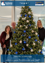 Bild zeigt drei Personen, die an einem Weihnachtsbaum stehen.