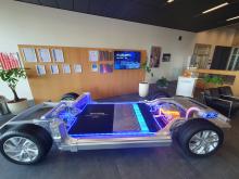 In einem Foyer ist der untere Teil des Chassis einen Elektrofahrzeuges zu sehen. Teile des Antriebsstranges, die Ladeelektrik und der Batteriespeicher sind eingebaut. Die Energieflüsse im Fahrzeug werden durch farbige LED-Bänder visualisiert.