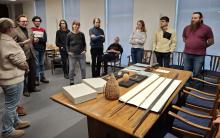 Mehrere Personen stehen um einen Tisch, auf dem viele Objekte stehen.