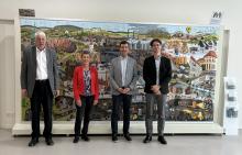 Vier Personen stehen vor einem großformatigen Wimmelbild