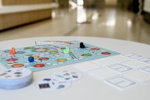 Brettspiel mit Spielplan, Spielfiguren, Würfel und Spielkarten auf hellem Tisch