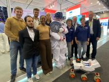 Gruppenfoto auf einer Messe, vorne ein Marsrover, hinten Menschen, davon eine Astronautin