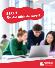 Drei junge Menschen sitzen an einem Tisch und schauen gemeinsam auf einen Laptop in einem hellen Raum mit großen Fenstern