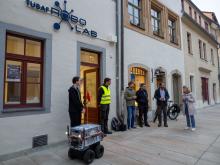 Eine Menschengruppe vor dem RoboLab in Freiberg verabschiedet einen Lieferroboter
